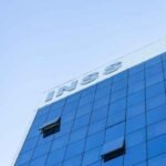 Fachada moderna de agência do INSS com revestimento em vidro espelhado azul, ilustrando previdência social, aposentadoria, benefícios e serviços públicos no Brasil.